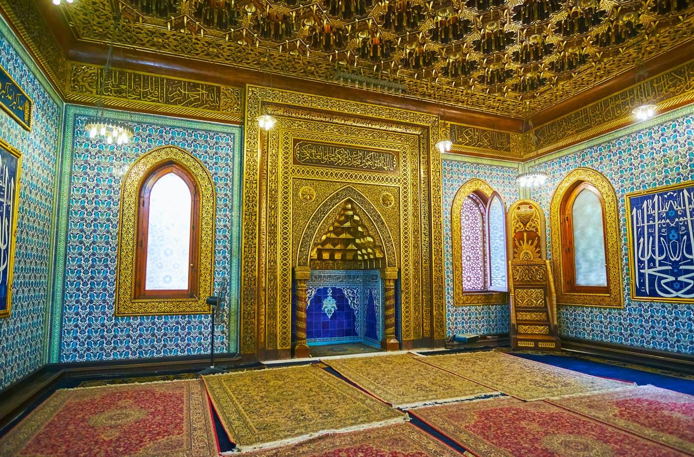 Cairo, Egypt - December 24, 2017:  Mihrab of Manial Palace mosque decorated with intricate golden patterns on carved wood, muqarnas in arch, bright blue tiles inside of niche, on December 24 in Cairo